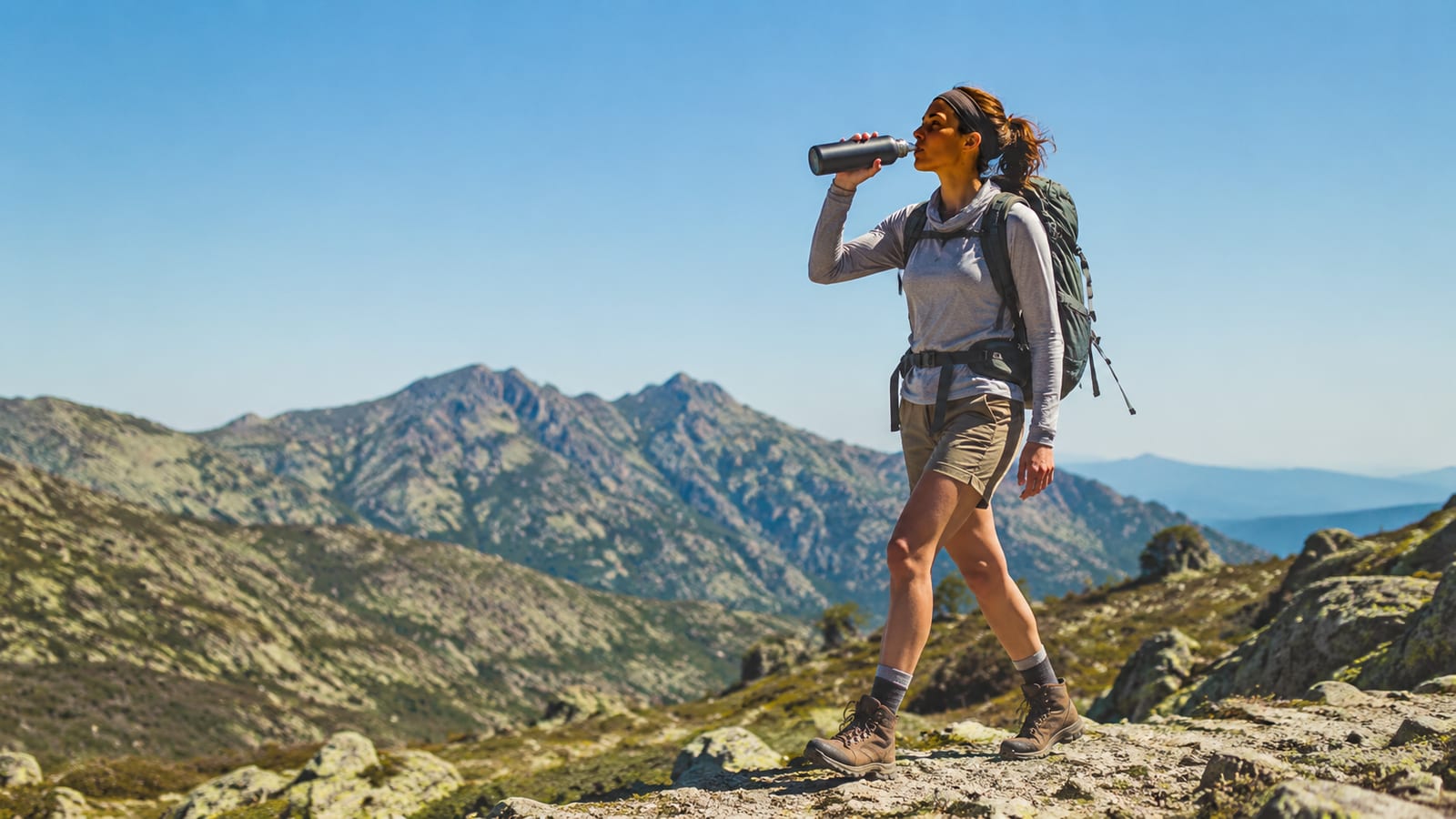 Hiker drinking from insulated water bottle on a rocky mountain trail during daytime