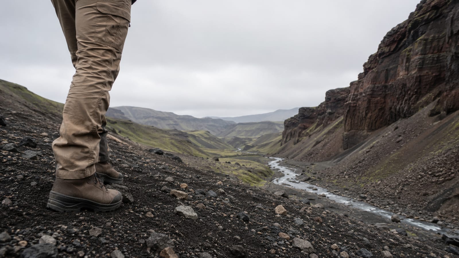 Hiker overlooking volcanic creek canyon with green moss-covered hills and black gravel terrain