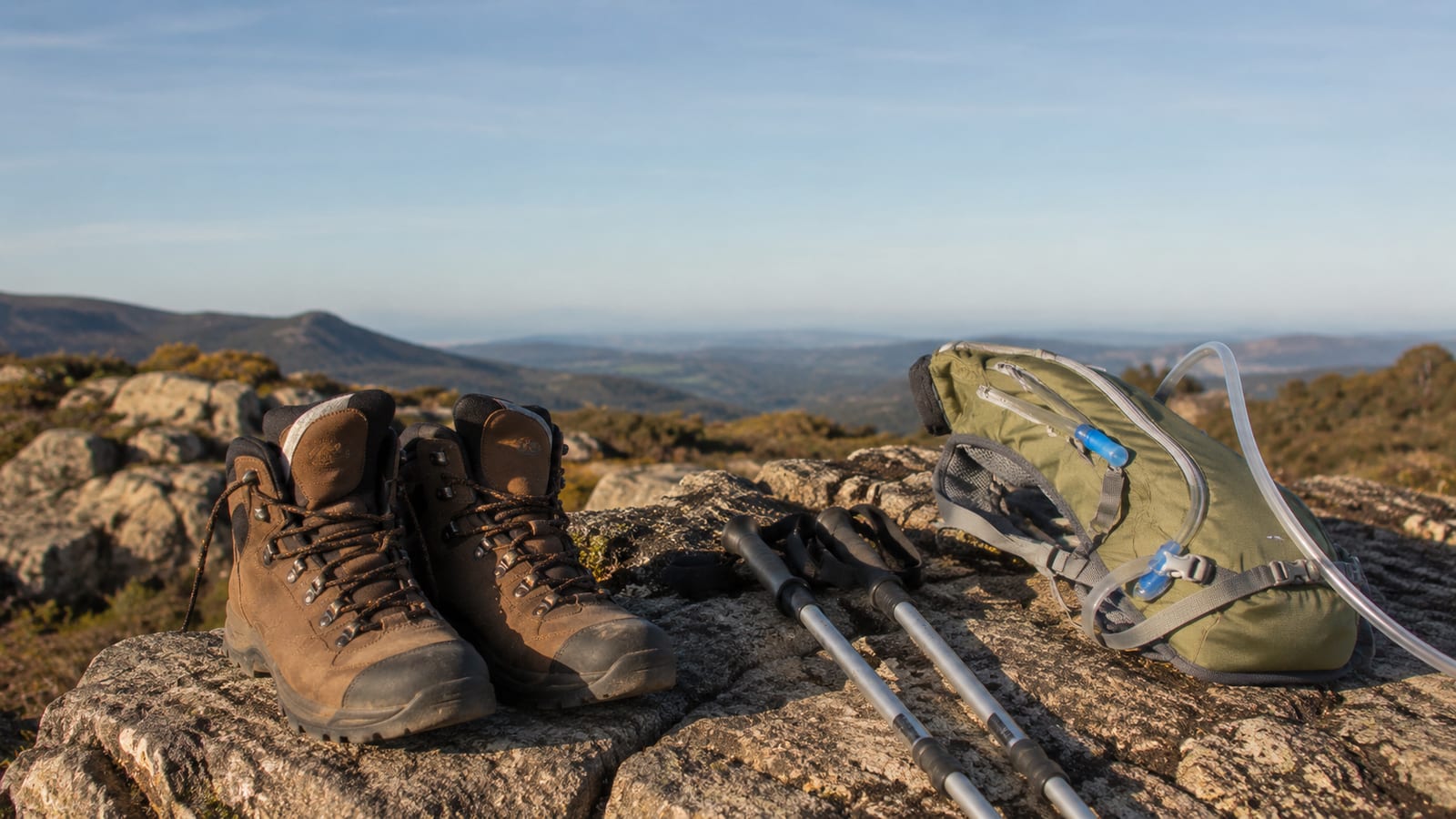 Hiking boots, trekking poles, and a green hydration pack resting on rocky terrain