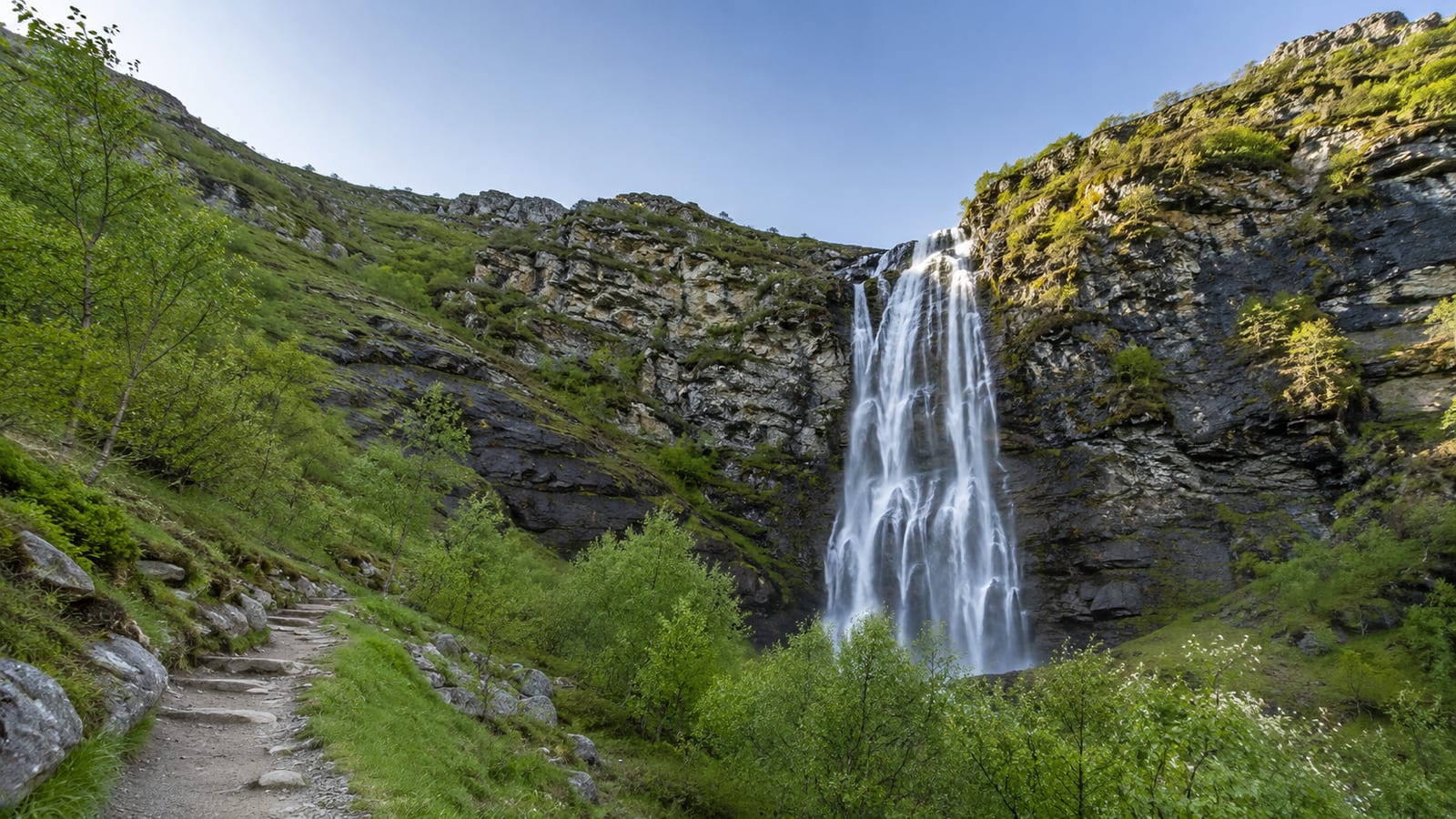 7 California trails with kid-friendly landmarks, waterfall cascading down rocky cliff beside a stone hiking path
