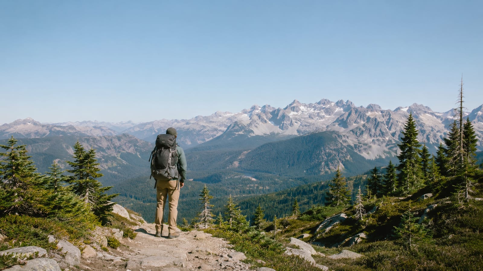 Best Banff Hiking Trails: 7 Hikes for Every Fitness Level, hiker with backpack overlooking snowy mountain range from ridge trail