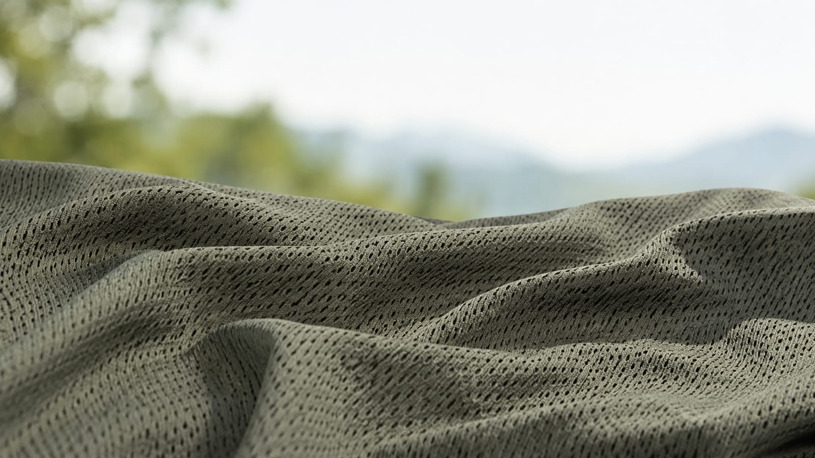 Close-up of textured gray breathable hiking shirt fabric outdoors with blurred mountain backdrop