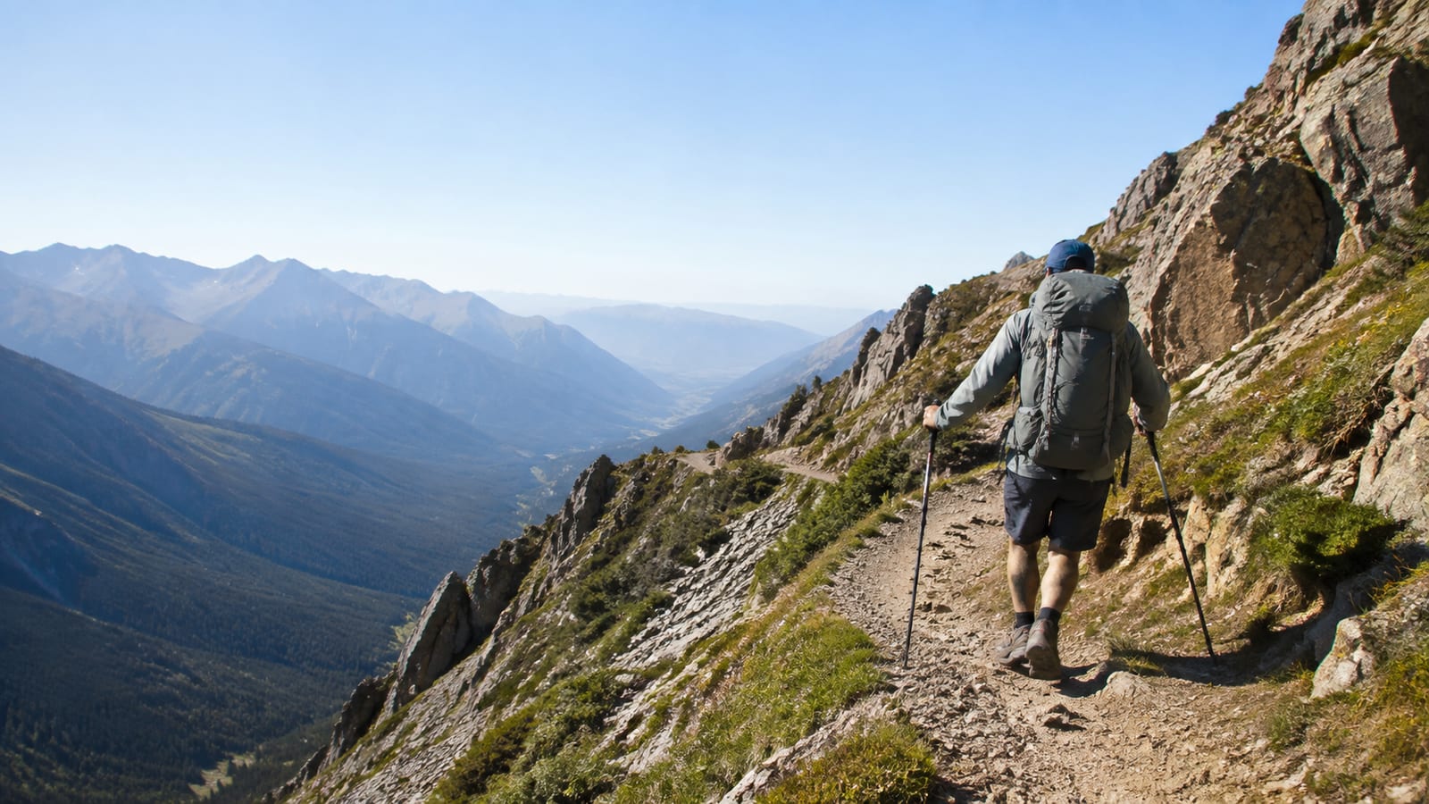Hiker seen from behind rounding a steep switchback with trekking poles carefully planted