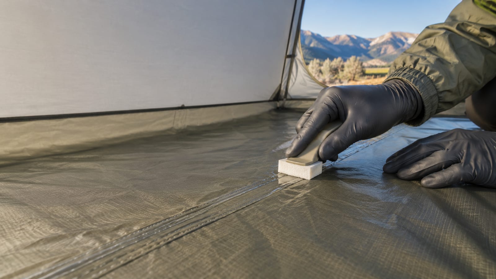 Gloved hands gently restoring a tent seam and waterproof coating with an unmarked applicator