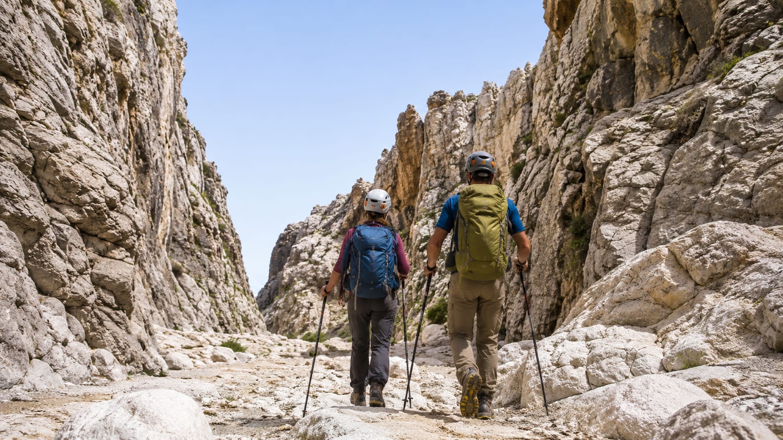 Two hikers navigating a limestone gorge with helmets, backpacks, and trekking poles